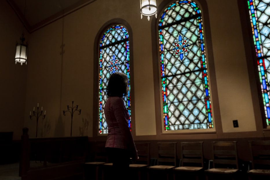 A woman looks at stained glass windows in a church