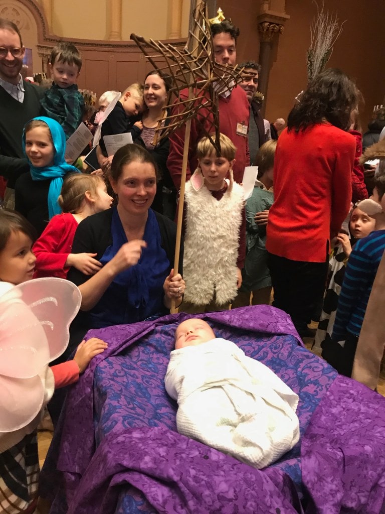 a young mother sitting next to her baby playing Jesus in the UnPageant, surrounded by church members