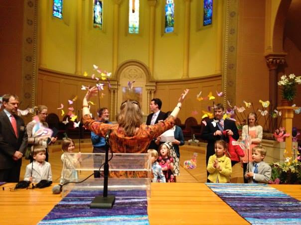 a woman conducts a multigenerational group of singers in the sanctuary